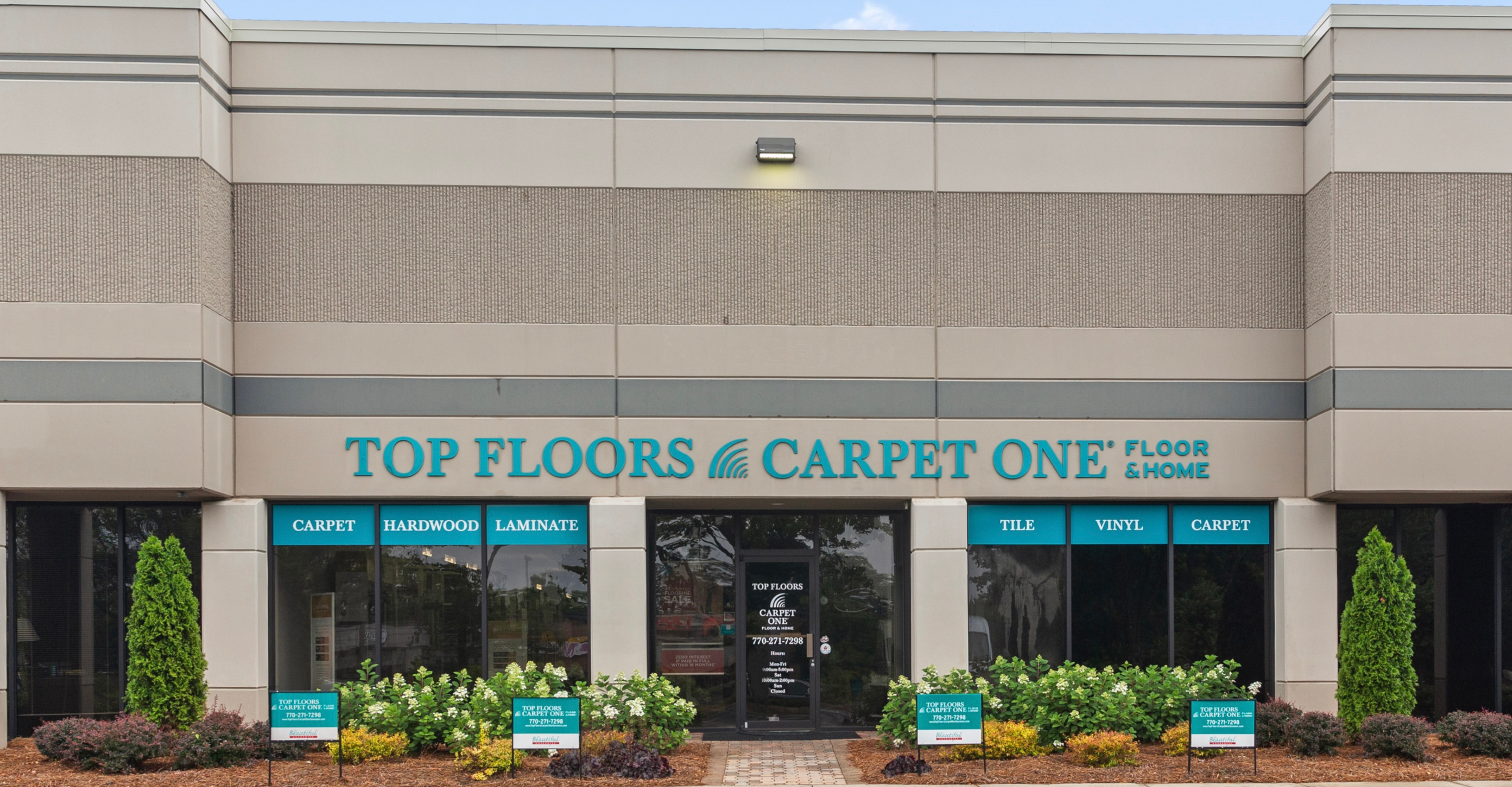 Top Floors Carpet One Floor & Home storefront in Gwinnett County, serving Northeast Metro Atlanta. Teal signage displays product offerings: Carpet, Hardwood, Laminate, Tile, and Vinyl. Beige exterior 