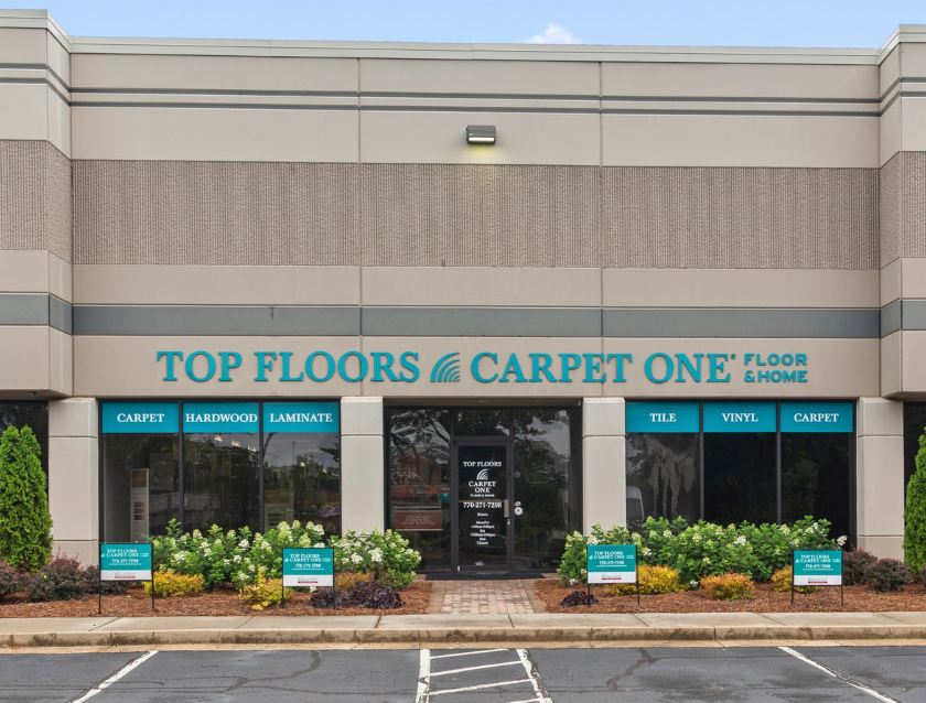 Top Floors Carpet One Floor & Home storefront in Suwanee, Georgia. Teal signage displays product offerings: Carpet, Hardwood, Laminate, Tile, and Vinyl. Professional flooring retailer serving Gwinnett